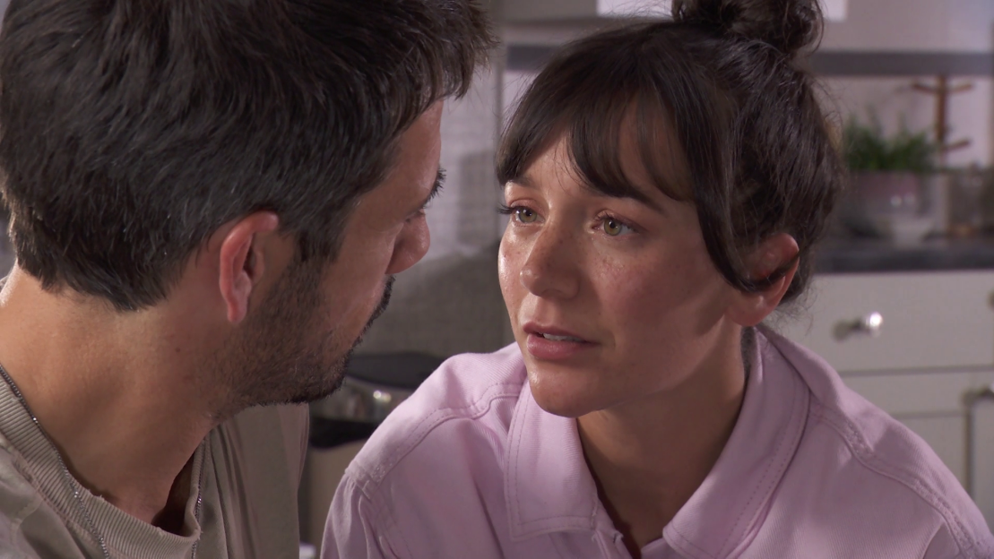 Still image from Hollyoaks showing a man and woman looking intently at each other.