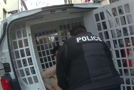 Police officer placing a shirtless man into a police van.