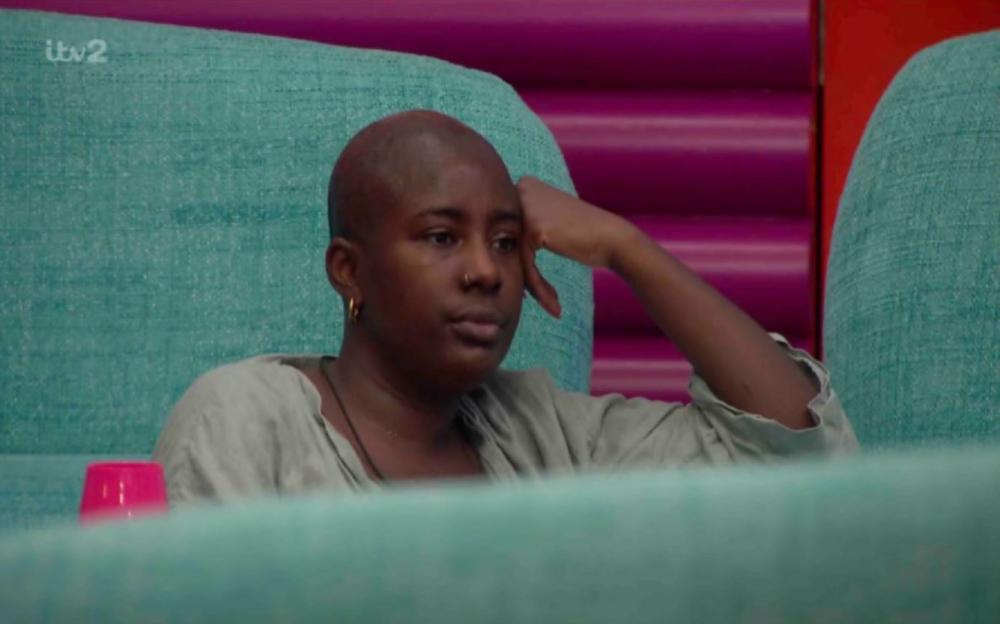 Feyisola looking emotional while sitting on a teal couch, resting her head on her hand.