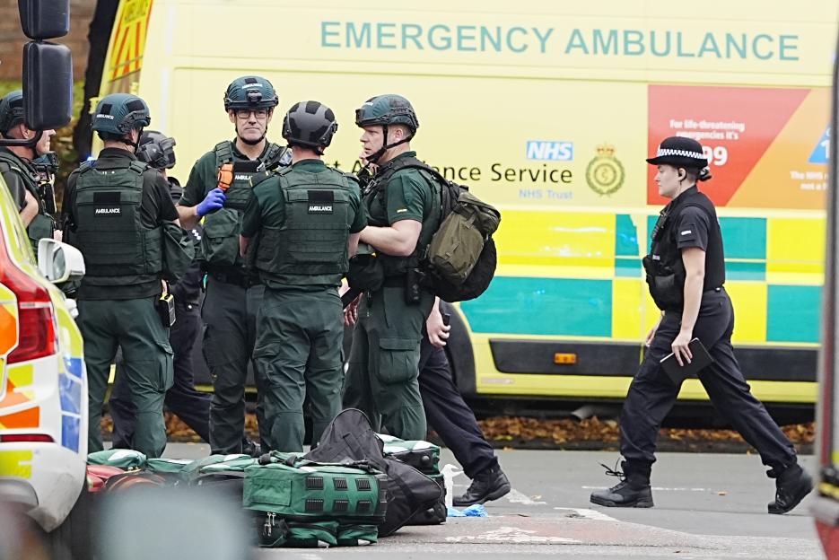 Emergency services personnel and a police officer at the scene of an incident with an ambulance in the background.