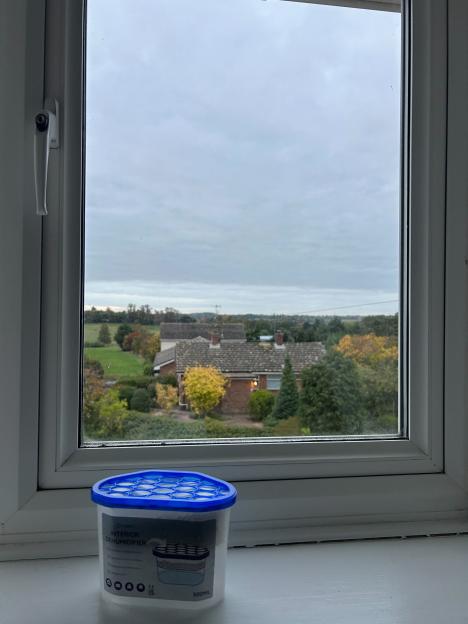 An interior dehumidifier sitting on a window sill with a view of houses and trees in the distance under a cloudy sky.