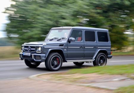 A dark gray Mercedes G-Wagon driving on a road.