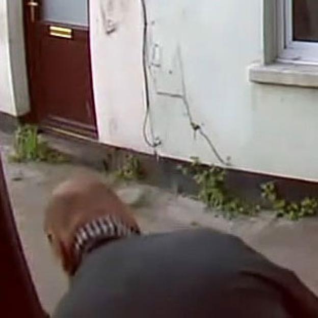 Video still of a man defecating on a doorstep.
