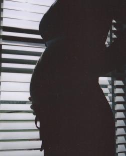 Silhouette of a pregnant person standing by a window.