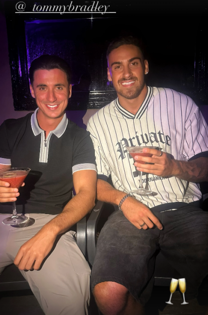 Two men sitting together, each holding a cocktail.