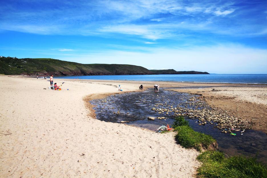 Beachgoers enjoying a sunny day at a sandy beach with a small stream.