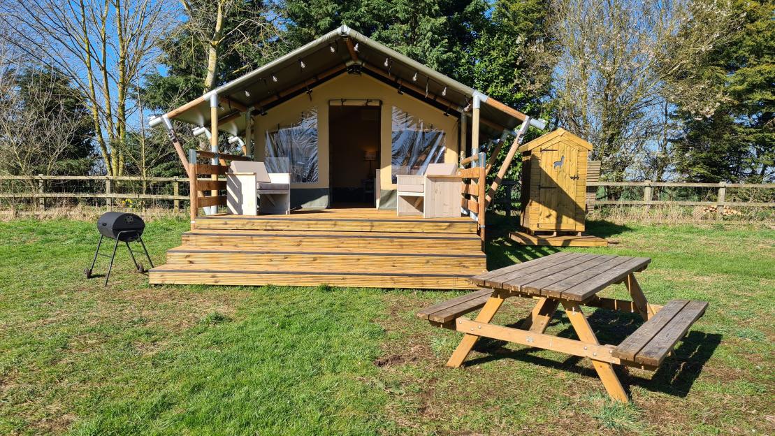 Glamping tent with picnic table and grill.