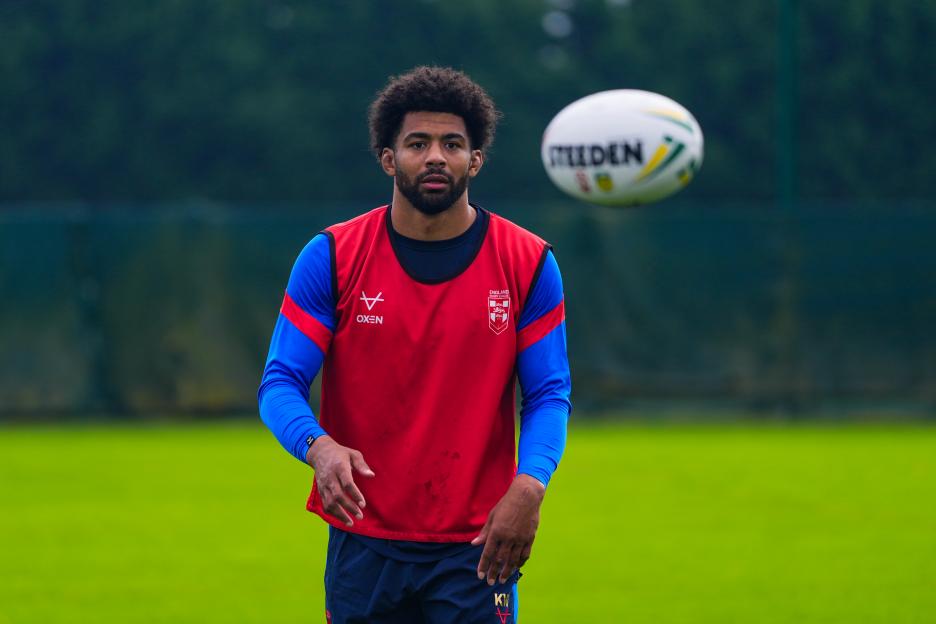 Kallum Watkins in a red and blue England rugby jersey with a rugby ball in the air.