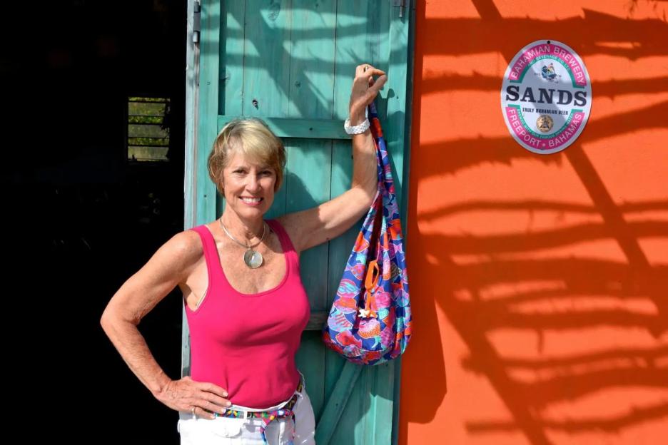 Woman standing by teal door with colorful bag.