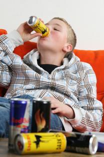 Teenager drinking energy drink surrounded by cans of energy drinks.