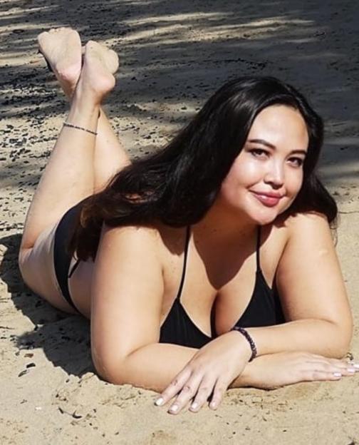 Woman in a black bikini lying on her stomach in the sand.