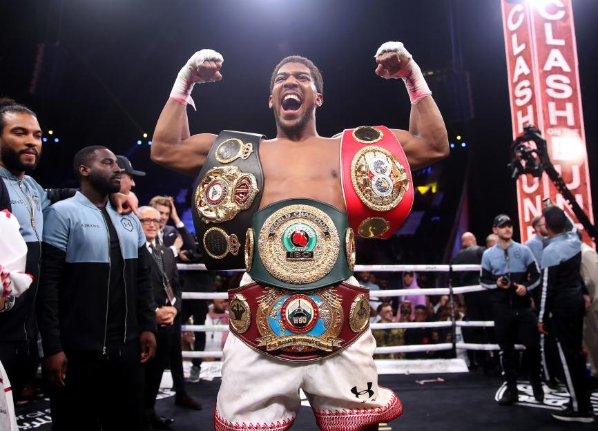 Anthony Joshua holding up his championship belts after a boxing match.