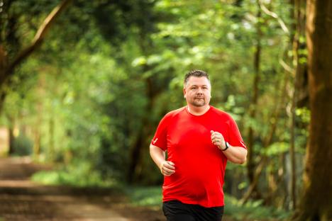 A man jogging through a sunlit forest.