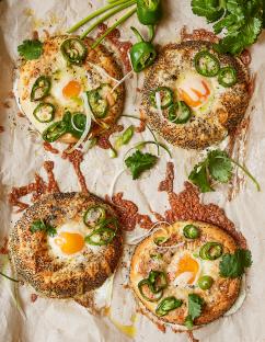 Four bagels topped with cheese, a fried egg, jalapeños, and cilantro.