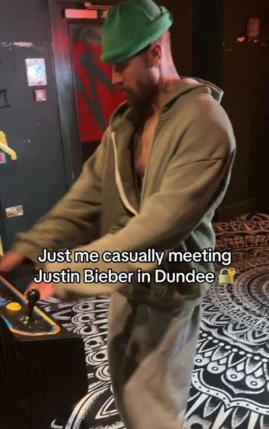 Justin Bieber playing an arcade game in a casual setting.