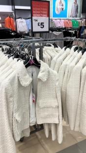 Cream-colored jackets on display at a Primark sale, reduced from £34 to £5.