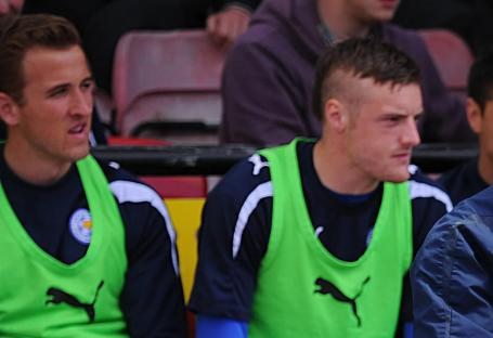 Nigel Pearson, Leicester City manager, speaks with another manager on the sidelines. Players look on from the bench.