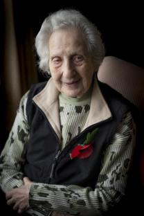 Portrait of a smiling elderly woman wearing a camouflage sweater and a poppy.