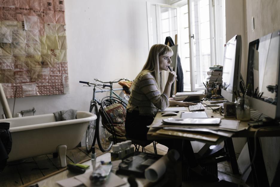 Young businesswoman working at a cluttered home office desk.