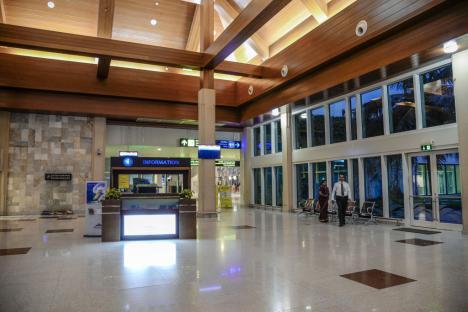 Empty airport terminal with information counter and two people waiting.