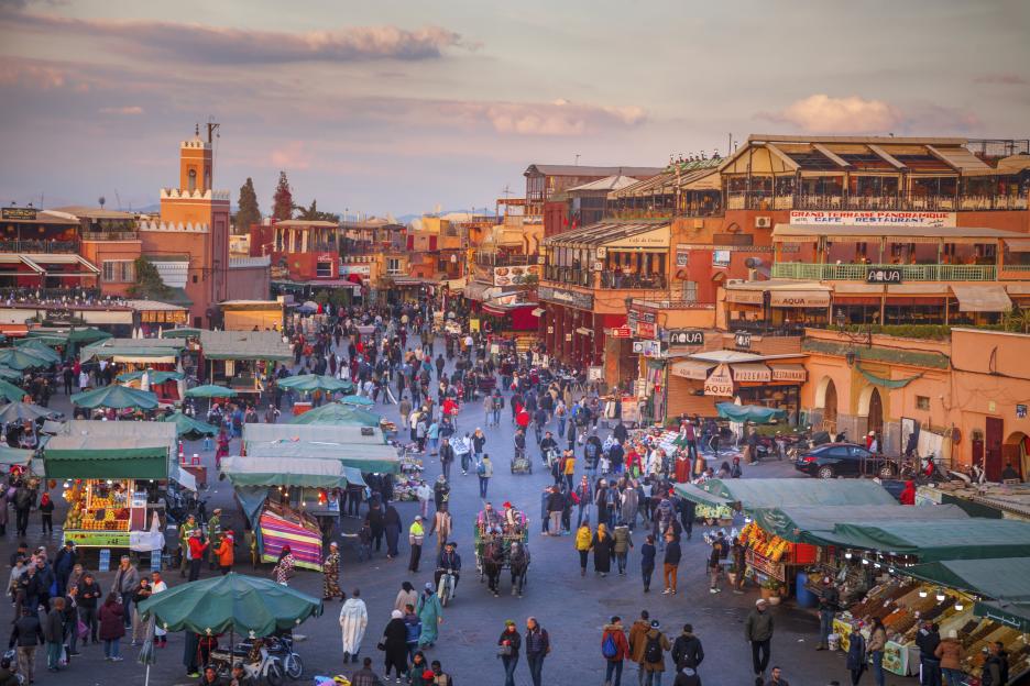 Jemaa el-Fnaa square in Marrakesh with many people, market stalls, and buildings with restaurants and cafes.