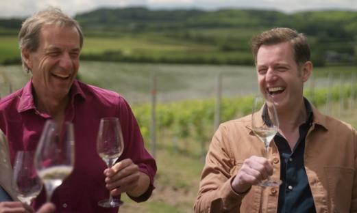 Matt Baker laughing while holding a glass of wine in a vineyard.