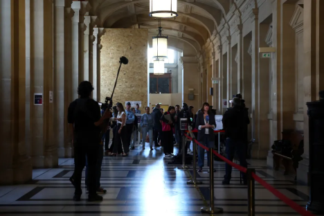 Reporters interviewing a woman in a long hallway with columns.