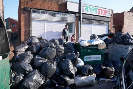 A large pile of black garbage bags overflowing near a building.