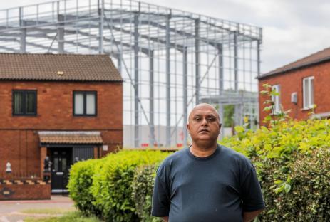 Man stands in front of a large warehouse under construction.