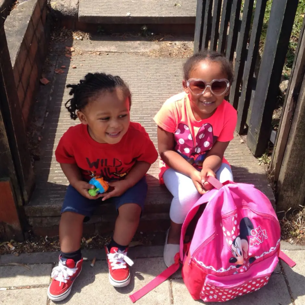 Two young children sitting on steps with a pink backpack.