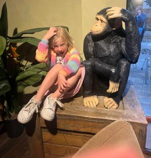 A young girl sits next to a chimpanzee statue at Chessington World of Adventures.