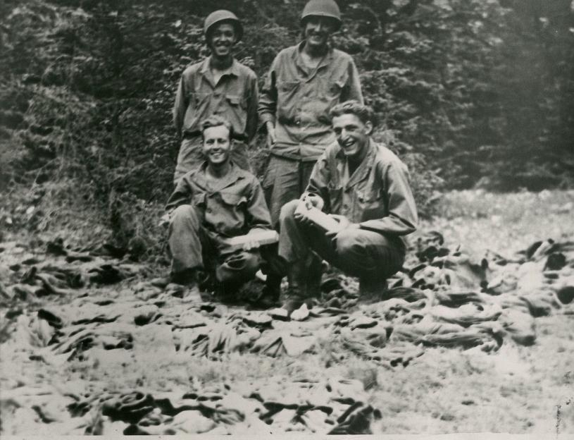 Four smiling soldiers in uniform posing in a wooded area.