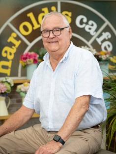 Ian Smith, actor who played Harold Bishop in Neighbours, sitting in front of Harold's Cafe sign.