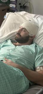Man in hospital bed with head bandage.