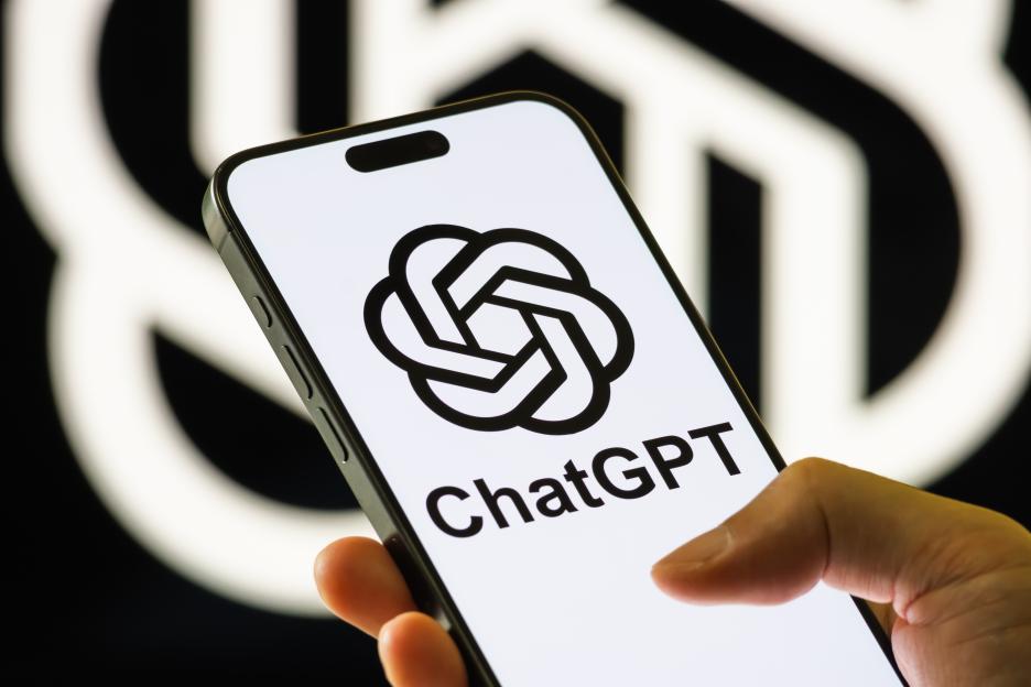 Photo illustration of a person holding a smartphone displaying the ChatGPT logo on its screen.