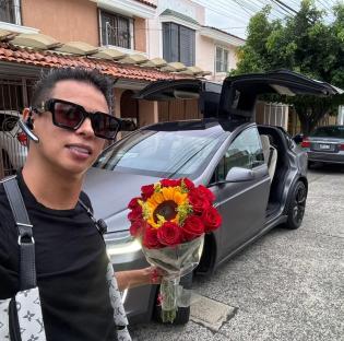 Photo of Alex Marin holding a bouquet of red roses and a sunflower in front of a Tesla.