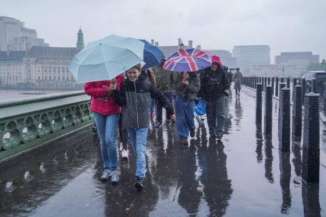 Pedestrians with umbrellas on Westminster Bridge in heavy rain.