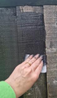 Hand applying dark paint to a wooden fence.