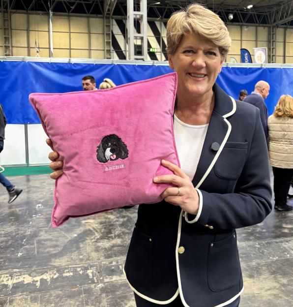 Lucy Bowes holding a pink pillow with an embroidered black and white dog and the name "Archie".