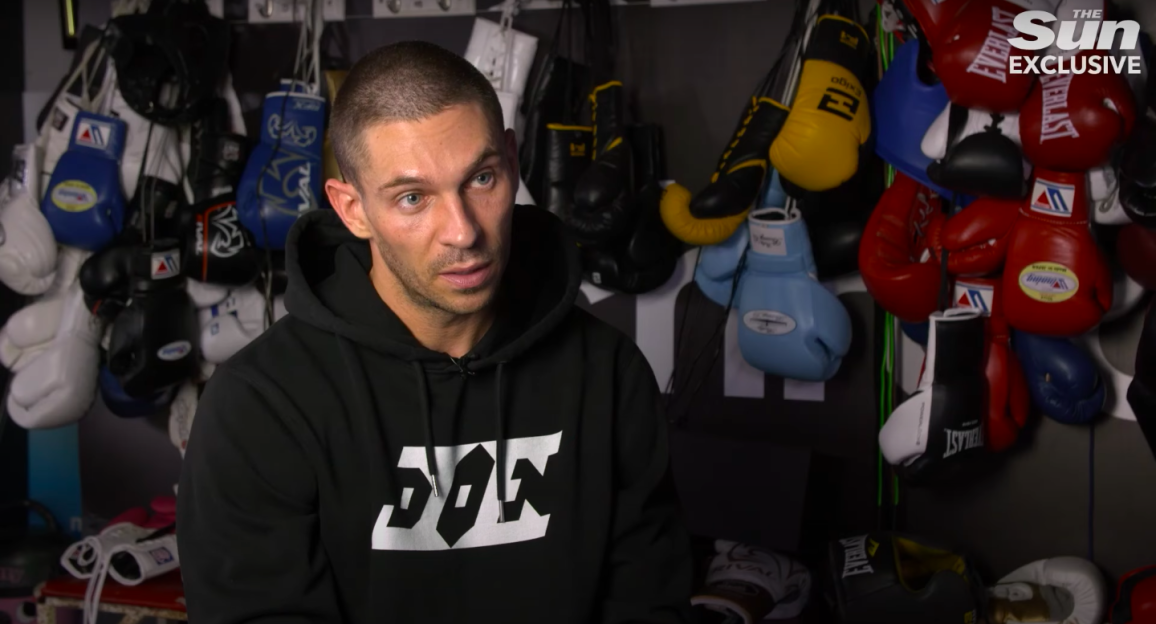 Man in black hoodie sits for interview in boxing gym.