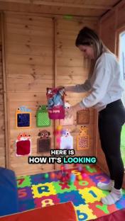 A woman adds colorful balls to a child's play area built inside a wooden shed.