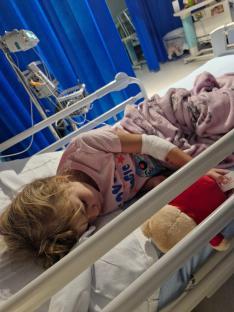 A young girl sleeping in a hospital bed with a teddy bear.
