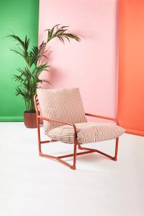 Red metal chair with striped cushions in front of a pink, green, and orange background.