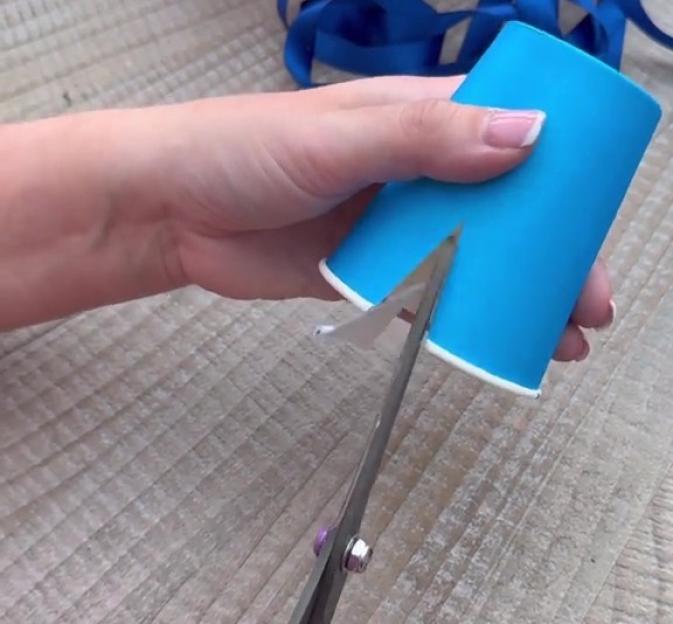 Hands cutting a blue paper cup.