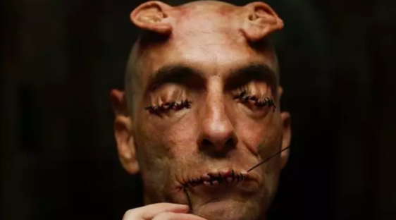 Close-up of a man with stitched eyes and mouth, and small horns on his head.
