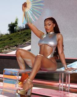 Megan Thee Stallion in a silver swimsuit holding a iridescent hand fan.