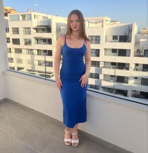 A young woman in a blue dress stands on a balcony.