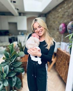 Woman holding a baby wearing a knitted cardigan.