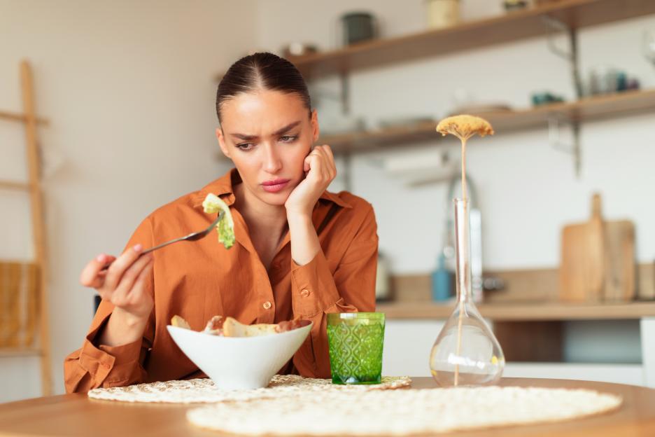 Woman with a sad expression looking at a forkful of salad.