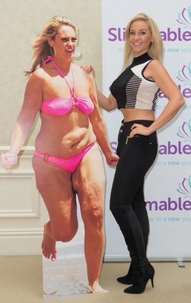 A woman in a black and white crop top and black pants stands next to a cardboard cutout of a woman in a pink bikini, with "Slimmable" branding in the background.